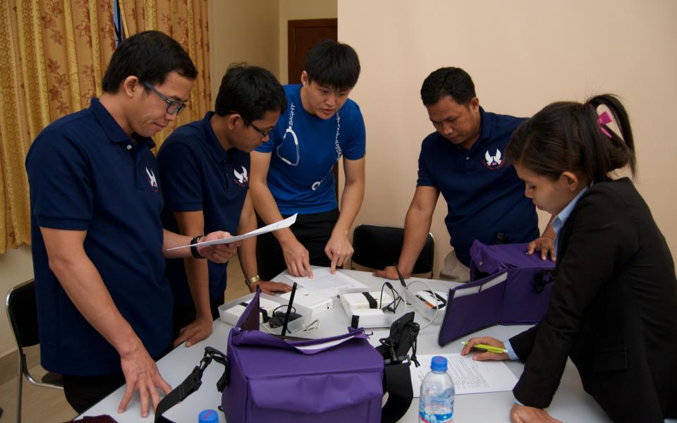 The student is demonstrating to the clinical staff in Cambodia how to use the mobile application of the electronic medical record system. 