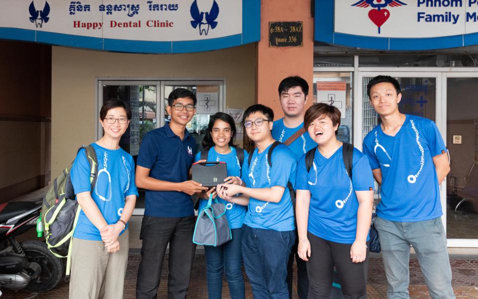 周教授和视野无界MedEasy的队员在One-2-One办公室门前向职员讲解MedEasy的伺服器。 One-2-One是柬埔寨当地的非政府组织，亦是视野无界成立后首批合作伙伴之一。该项目赢得2016年莱斯360°第六届本科生全球健康科技设计比赛第一名。